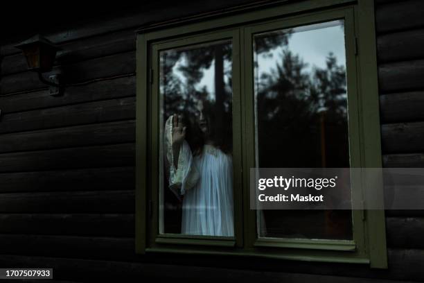 female ghost looking through glass window of haunted cabin - fantasma foto e immagini stock