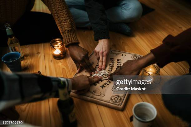 multiracial male and female friends using ouija board in house - séance photo stock pictures, royalty-free photos & images