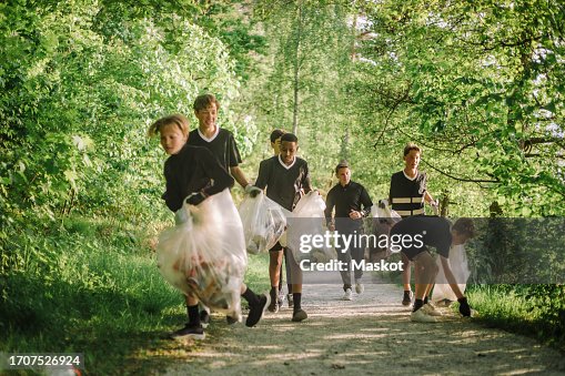 Boys and coach plogging on footpath amidst green plants Boys and coach plogging on footpath amidst green plants