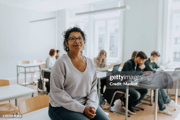 portrait of female professor sitting on desk in classroom - lecturer stock pictures, royalty-free photos & images