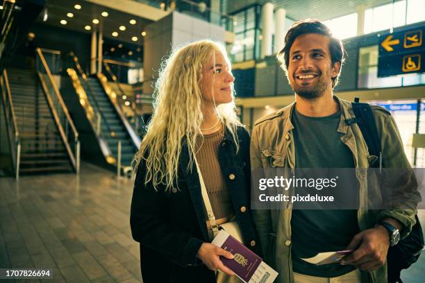 young adult couple at the airport, looking for their departure gate, heading away on a weekend vacation. - airport couple stockfoto's en -beelden