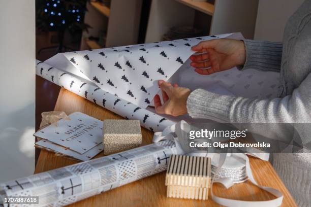 woman's hands in a grey jumper wrapping christmas presents on a table - christmas gift bag stock pictures, royalty-free photos & images