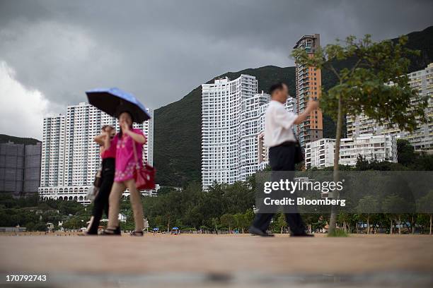 People walk on a waterfront promenade at Repulse Bay beach in front of residential buildings in Hong Kong, China, on Sunday, June 16, 2013. A...