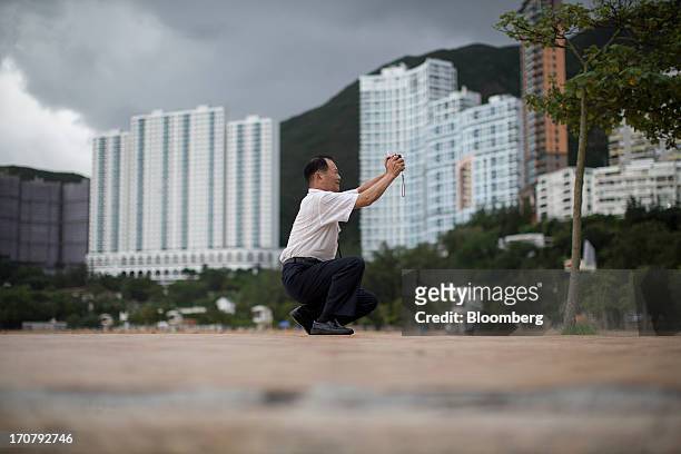 Man takes a photograph on a waterfront promenade at Repulse Bay beach in Hong Kong, China, on Sunday, June 16, 2013. A shortage of housing, low...