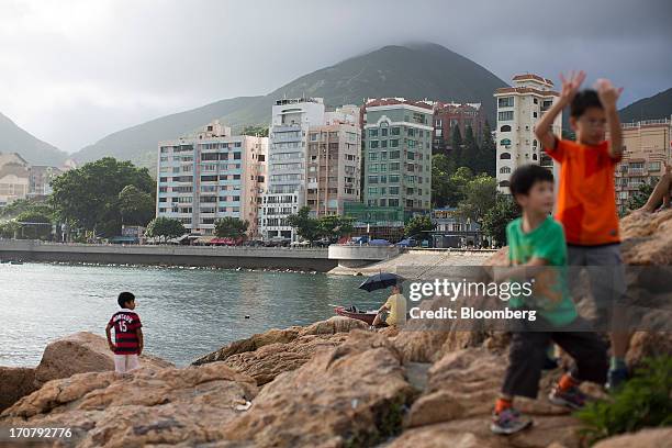 Children play on rocks by the waterfront across from residential buildings in the Stanley area of Hong Kong, China, on Sunday, June 16, 2013. A...