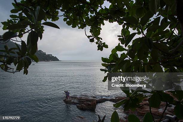 Two men fish on rocks on the waterfront in the Stanley area of Hong Kong, China, on Sunday, June 16, 2013. A shortage of housing, low mortgage costs...