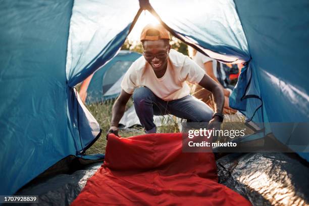 young smiling man setting up sleeping bag in camping tent - sleeping bag stock pictures, royalty-free photos & images