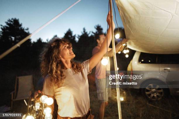 junges paar stellt lichterketten auf, um ihren campingplatz nachts zu dekorieren und zu beleuchten - installation art stock-fotos und bilder