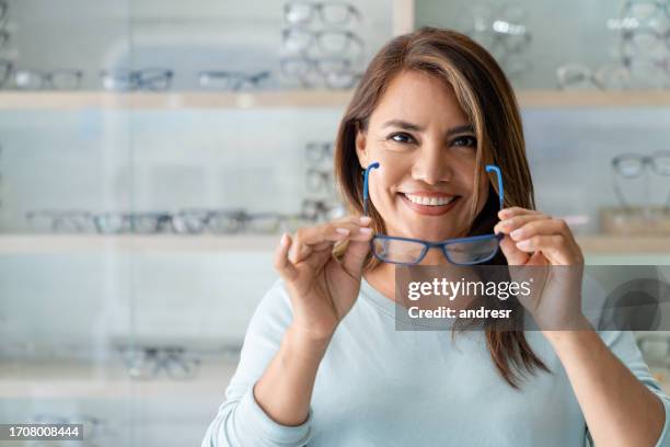 happy woman trying on new glasses at the optician's shop - bril stockfoto's en -beelden