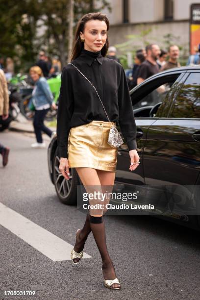 Mary Leest wears a black shirt with black turtleneck top underneath, gold mini skirt, black socks, gold sandals and silver metal bag, outside...