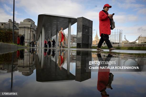 Pedestrians reflect in a puddle while walking in Moscow on October 5, 2023.