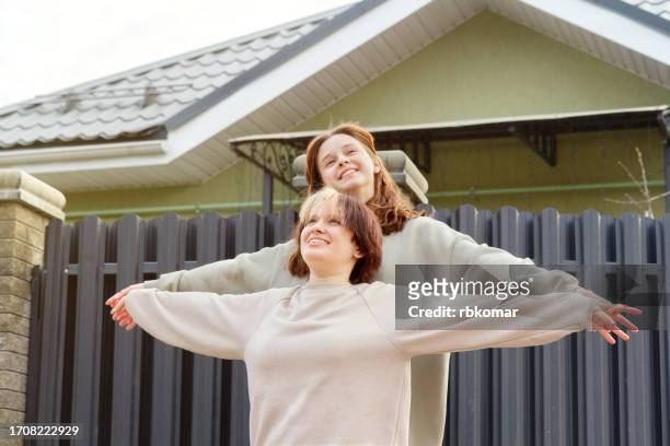 happy teen girls with arms outstretched looking up near the house - teen lesbian stockfoto's en -beelden