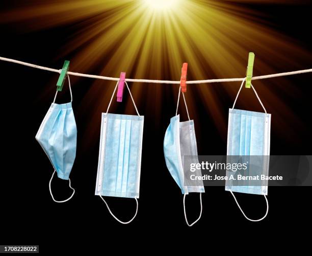 blue medical face mask hanging on the clothesline drying in the sun on a black background. - virus organism stock pictures, royalty-free photos & images