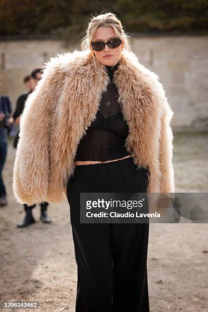 Toni Garrn wears a black sheer top, black trousers and nude fur jacket, outside Givenchy, during the Womenswear Spring/Summer 2024 as part of Paris...