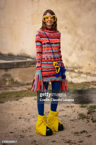 Guest wears a colorful knitted mini dress, blue tights, yellow puffed boots, yellow sunglasses and knitted bag, outside Givenchy, during the...