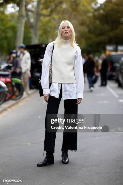 Model is seen wearing a white long-sleeves shirt, a white turtleneck sleeveless swearer, black wide leg jeans, a black bag and black leather boots...