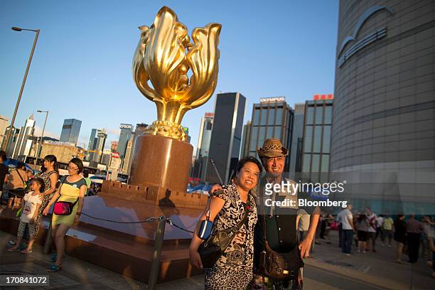 Couple pose for photographs in front of a sculpture of a gilded bauhinia at Golden Bauhinia Square in Hong Kong, China, on Tuesday, June 18, 2013. A...