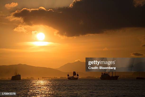 The Aqua Luna junk, a tour boat operated by Aqua Restaurant Group, center, sails in Victoria Harbor as the sun sets in Hong Kong, China, on Tuesday,...