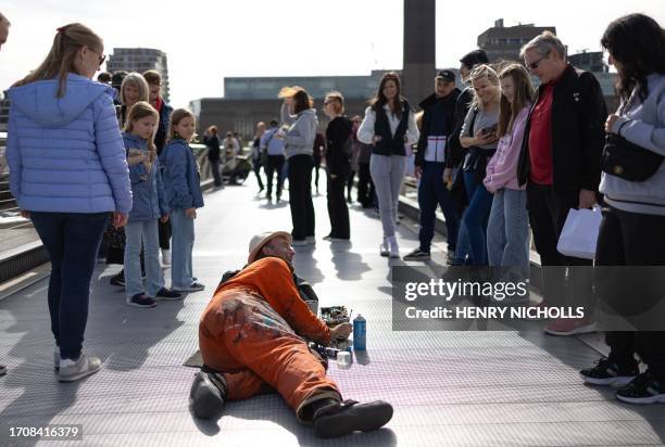 Pedestrians chat with artist Ben Wilson as he continues work on his project of painting on discarded pieces of chewing gum that have been left on the...