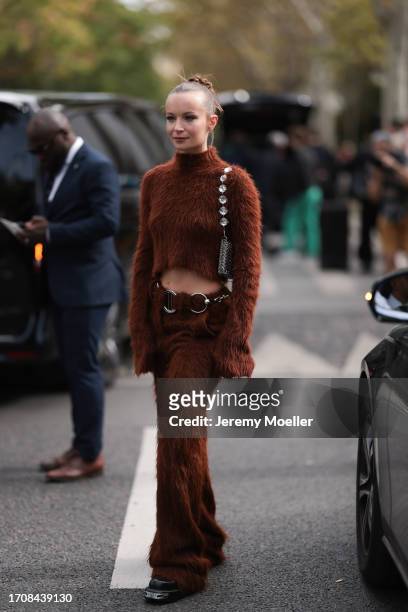 Diane Rouxel is seen wearing a brown crop turtleneck sweater and brown fur pants, along with a silver chain belt and a silver handbag with silver...