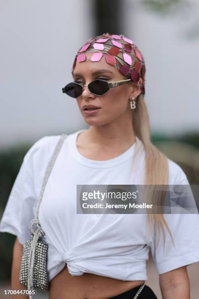 Fashion Week Guest is seen wearing a headpiece made of pink metal plates by Rabanne, silver earrings, sunglasses by Celine, a white T-shirt with knot...