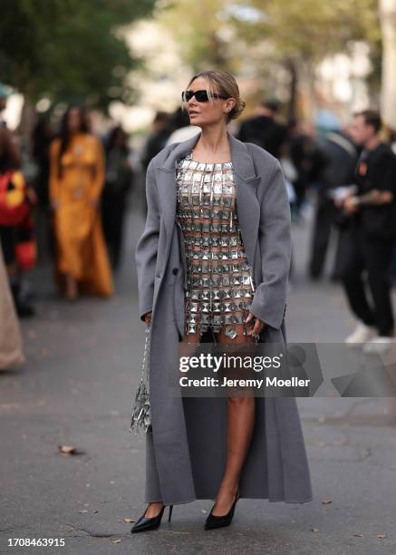 Veronica Ferraro is seen wearing she wears a long grey wool coat with shoulder pads, a short silver dress made of metal plates and a silver handbag...