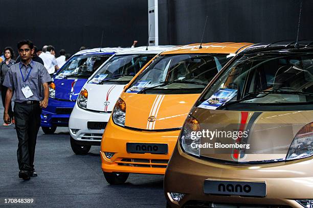 An employees walk past a line of Tata Motors Ltd. Nano automobiles on display during a media event in Pune, India, on Wednesday, June 19, 2013. Tata...