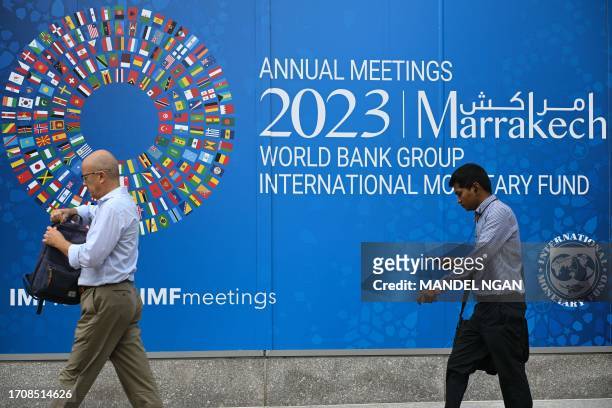Pedestrians walk past a billboard announcing the World Bank Group and International Monetary Fund annual meetings, on the side of the International...