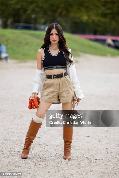 Heart Evangelista wears beige shorts, knee high white socks, brown boots, red bag, black white cropped top, jacket, black belt outside Loewe during...