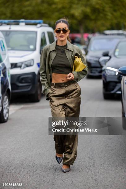 Camila Coelho wears green olive khaki cropped top, silk pants, button up shirt, yellow bag, sunglasses, pointed heels outside Loewe during the...