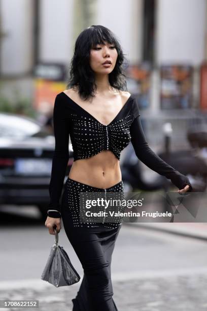 Guest is seen wearing a black cropped long sleeves studded sweater with the matching low-waist skirt, black leather boots and a silver metal mesh bag...