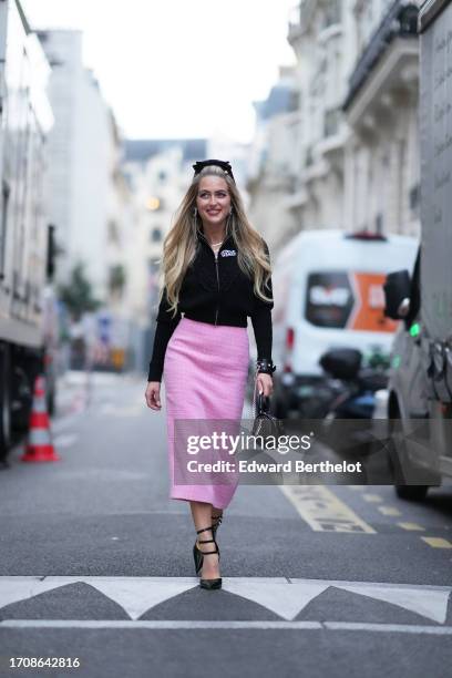 Emili Sindlev wears a black headband, a black cardigan, a pink midi tweed skirt with checked embroidered patterns, a black bag, black pointed shoes,...