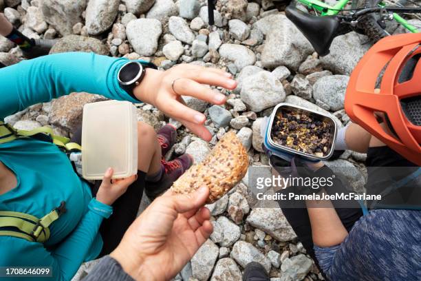 gruppe von mountainbikern, die gesunde snacks auf felsigem flussbett teilen - wildnisgebiets name stock-fotos und bilder