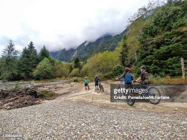 vielfältige multirassische mehrgenerationen-mountainbike-gruppe, die das flussufer erkundet - wildnisgebiets name stock-fotos und bilder