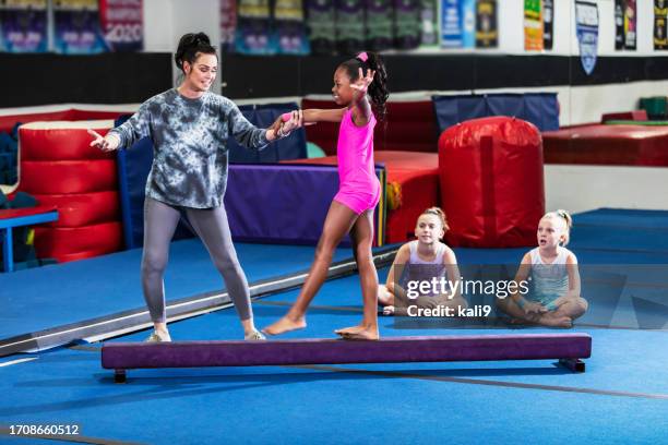 entrenador de gimnasia ayuda a una niña a practicar la barra de equilibrio - barra de equilibrio fotografías e imágenes de stock