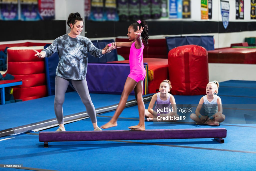 Gymnastics coach helps young girl practice balance beam