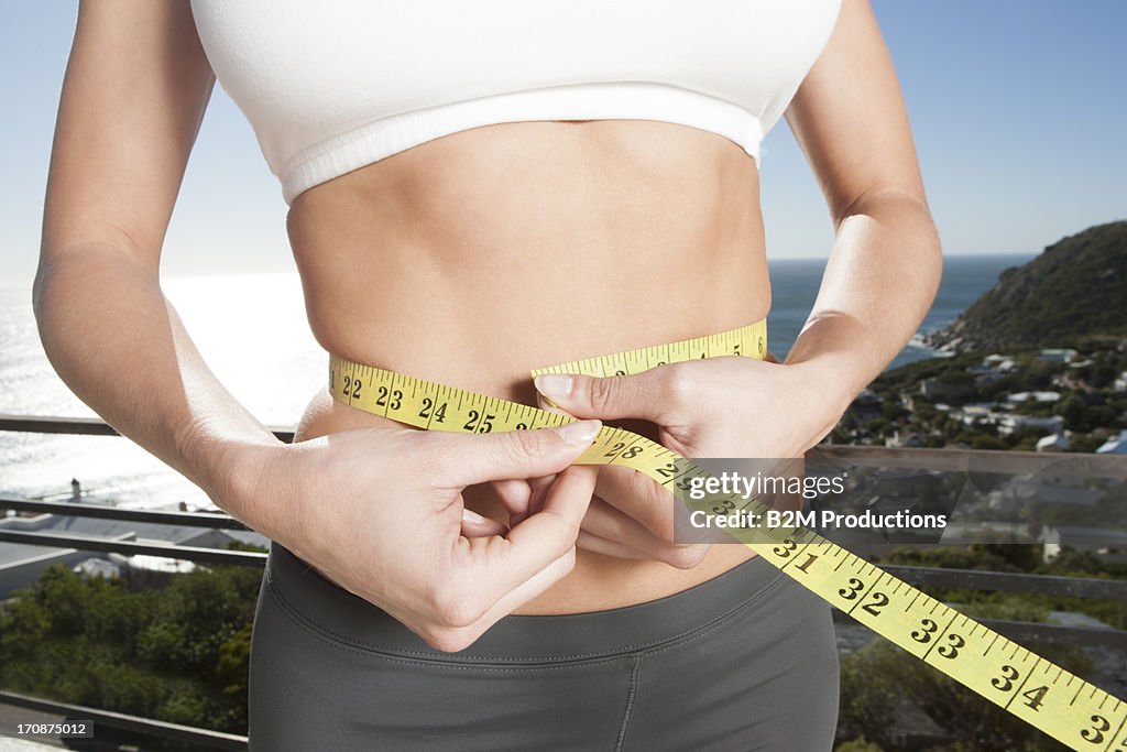 Close-up of woman measuring her waistline