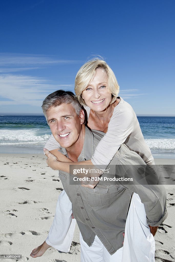 Senior man piggybacking his wife at beach