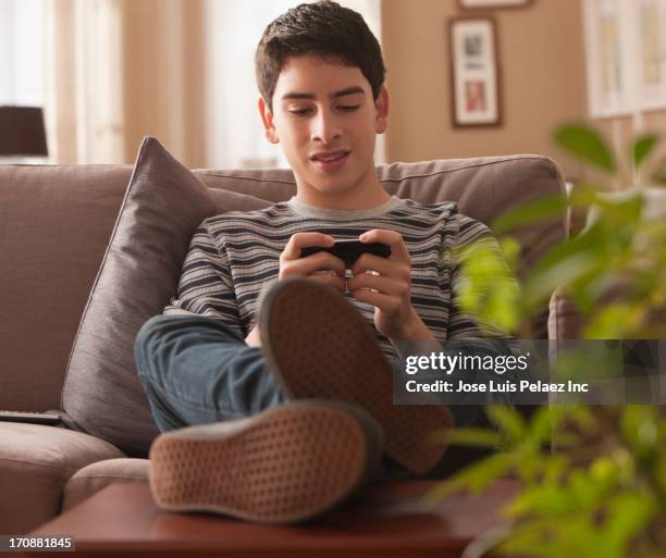 hispanic boy using cell phone on sofa - teenage boy playing playstation stock pictures, royalty-free photos & images