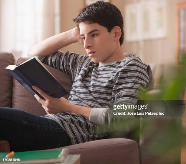 hispanic boy reading book on sofa - boy reading a book stock-fotos und bilder