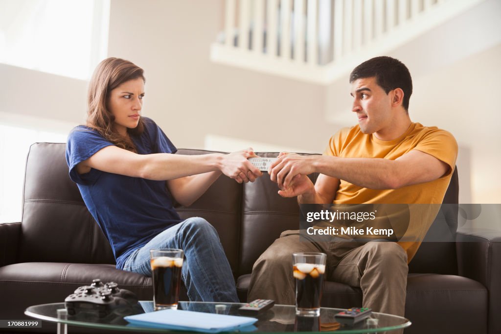 Couple arguing over remote on sofa