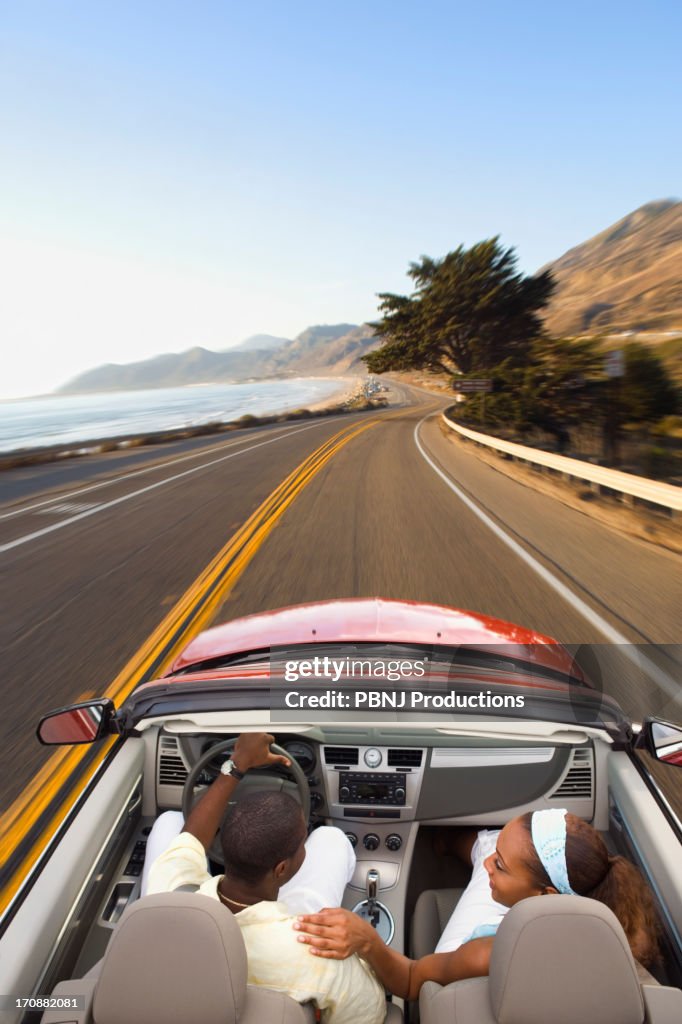 Couple driving convertible on coastal road