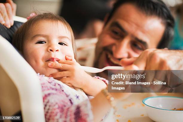 hispanic father feeding daughter in high chair - baby being fed stock pictures, royalty-free photos & images