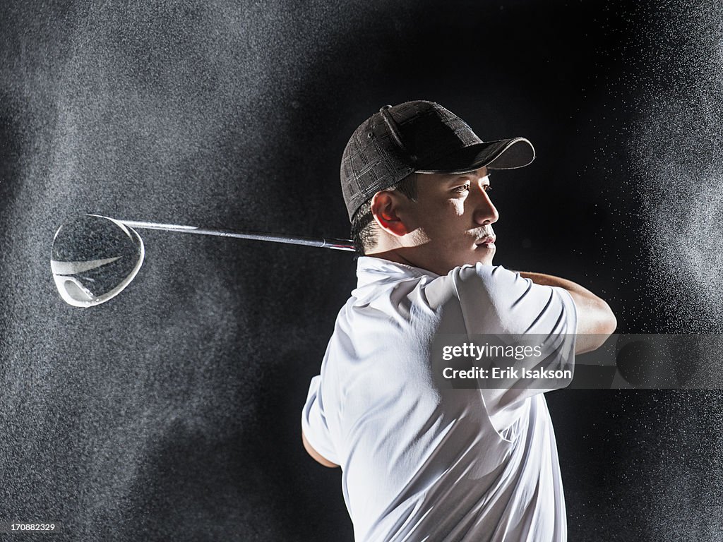 Asian golf player swinging club in rain