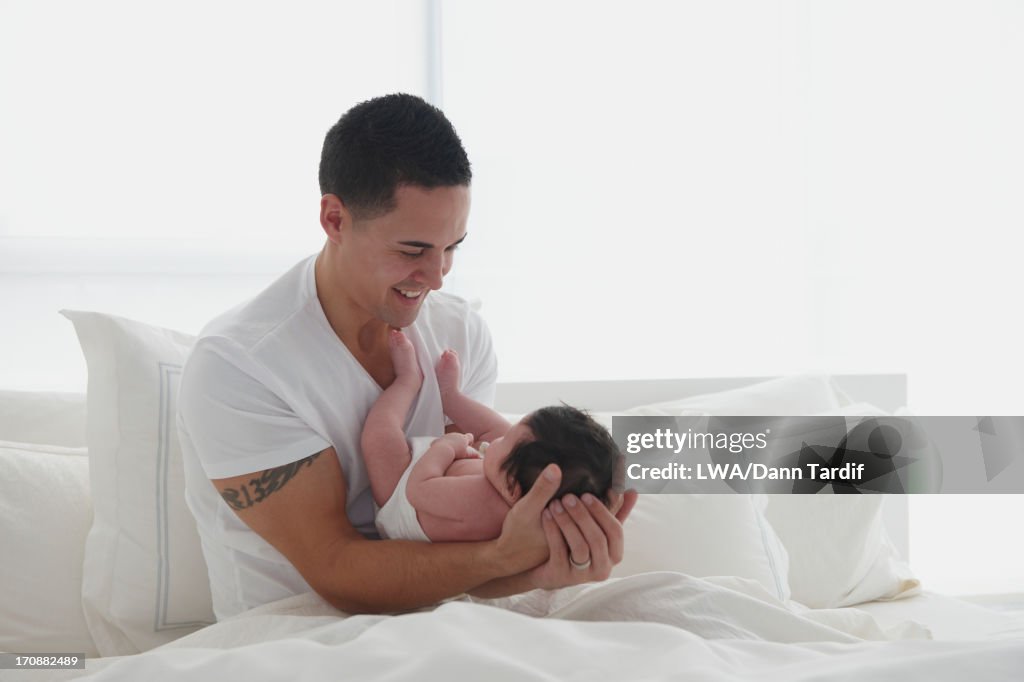 Hispanic father holding baby in bed