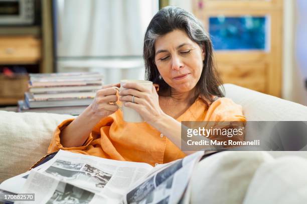 older hispanic woman reading newspaper on sofa - mature women coffee stock pictures, royalty-free photos & images