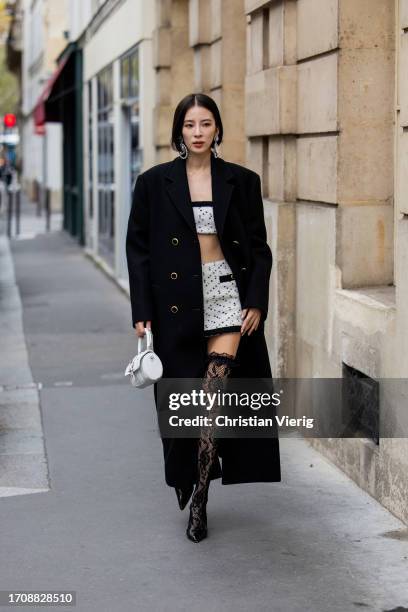 Irene Kim wears white cropped top, mini skirt, laced over knees tights, black coat, white bag outside Alessandra Rich during the Womenswear...