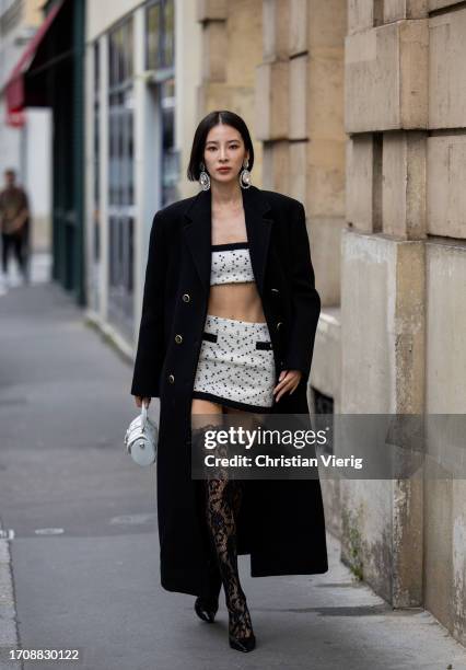Irene Kim wears white cropped top, mini skirt, laced over knees tights, black coat, white bag outside Alessandra Rich during the Womenswear...