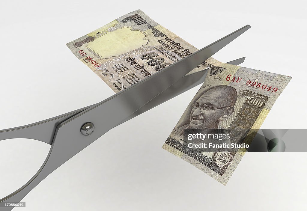 Scissor cutting Indian five hundred Rupee note representing concept of cost cutting