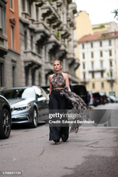 Guest wears earrings, a light grey with a black floral pattern chiffon crop top with American armholes, a matching vaporous long bow at the waist,...